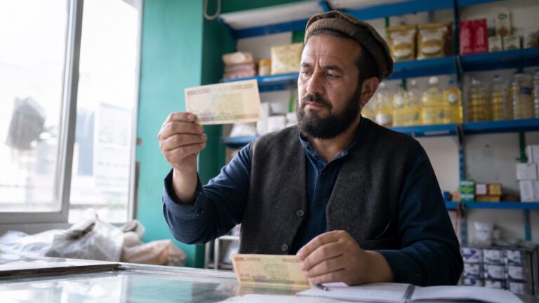 دکان‌دار افغان در حال بررسی یک اسکناس مشکوک در نور مناسب